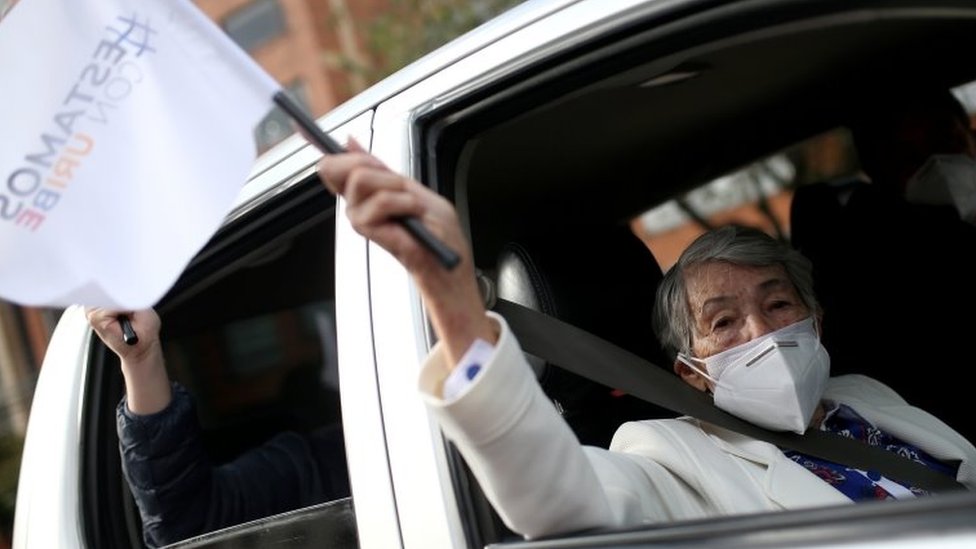 Un partidario de Álvaro Uribe, ex presidente y legislador de Colombia, usa una mascarilla y sostiene una bandera que dice 