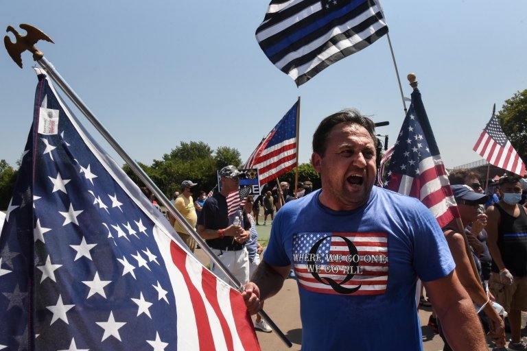 Человек в футболке в поддержку QAnon на митинге с флагами США