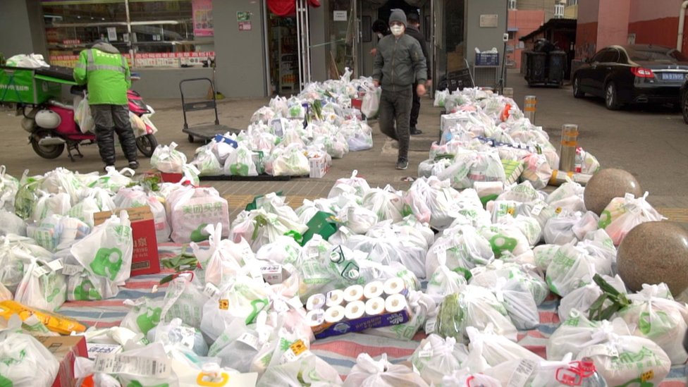 Pilhas de sacolas de mantimentos são colocadas no chão do lado de fora de um mercado de Pequim aguardando entregadores