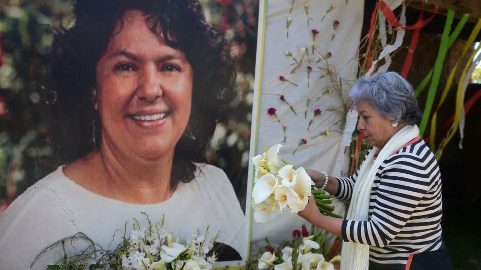 Una mujer deja flores antes un mural sobre Berta Cáceres