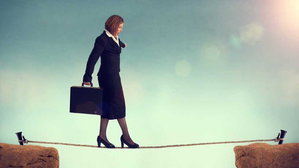 El momento escogido no es ninguna garantía de que no vayamos a fallar en el intento. Mujer trajeada camina sobre una cuerda entre dos picos.