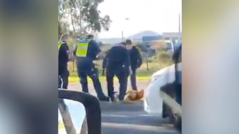 Четверо полицейских стоят над человеком, лежащим на земле во время ареста