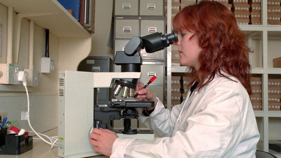 Una médico patólogo usando un microscopio.