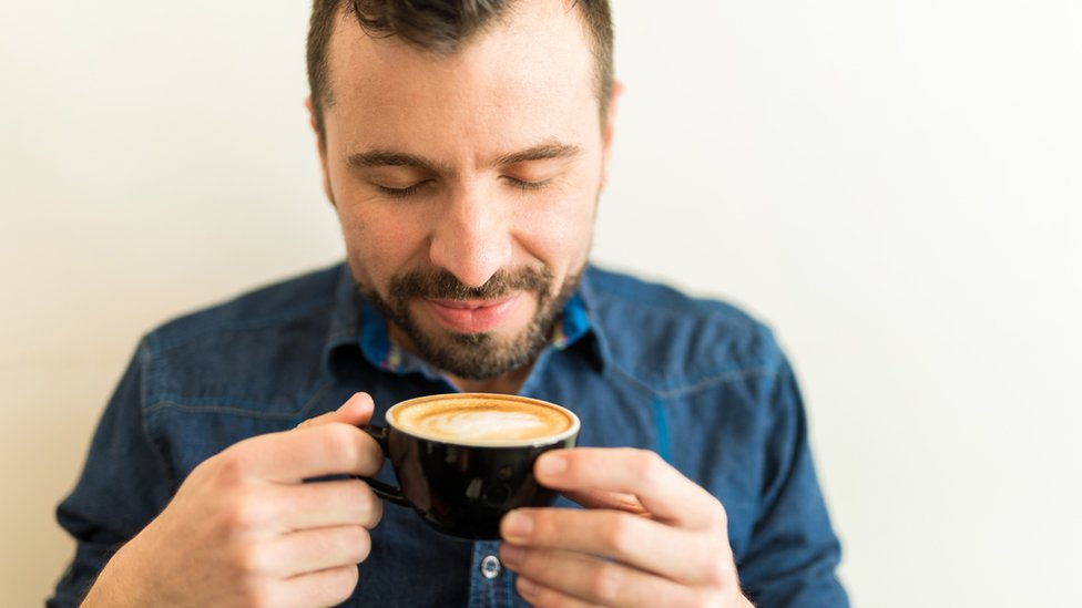 Hombre joven con los ojos cerrados inhala el aroma de una taza de café en sus manos