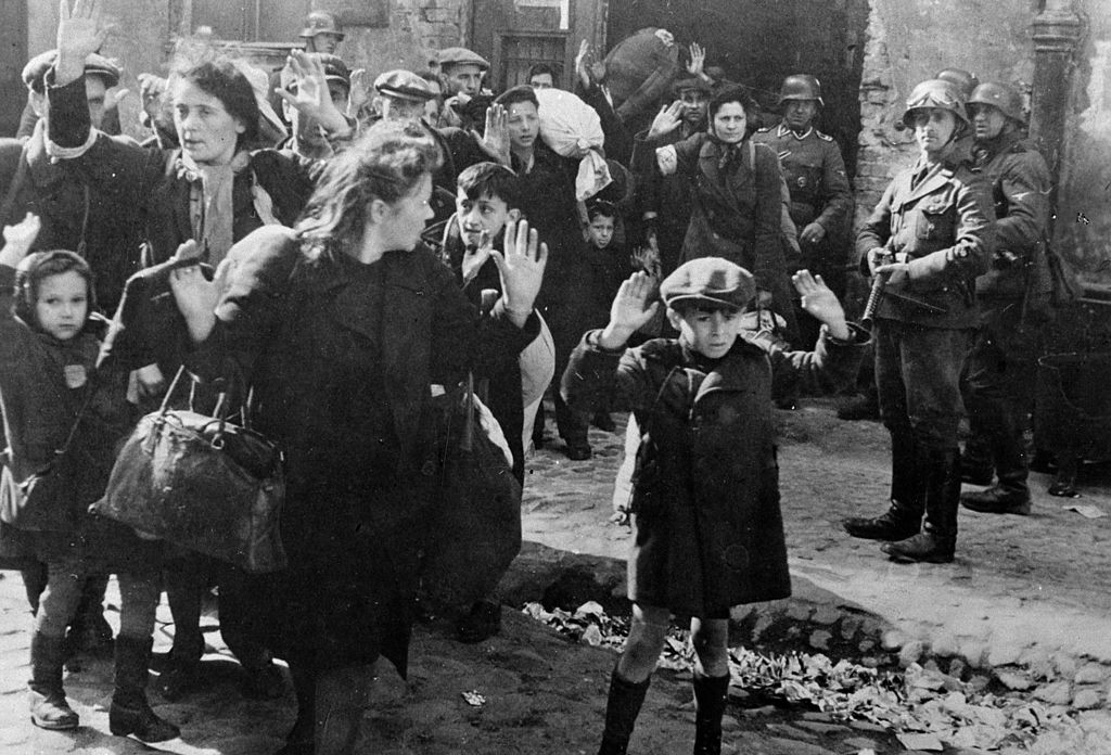 A group of Jews are forced by Nazi soldiers to walk in line in the Warsaw ghetto.
