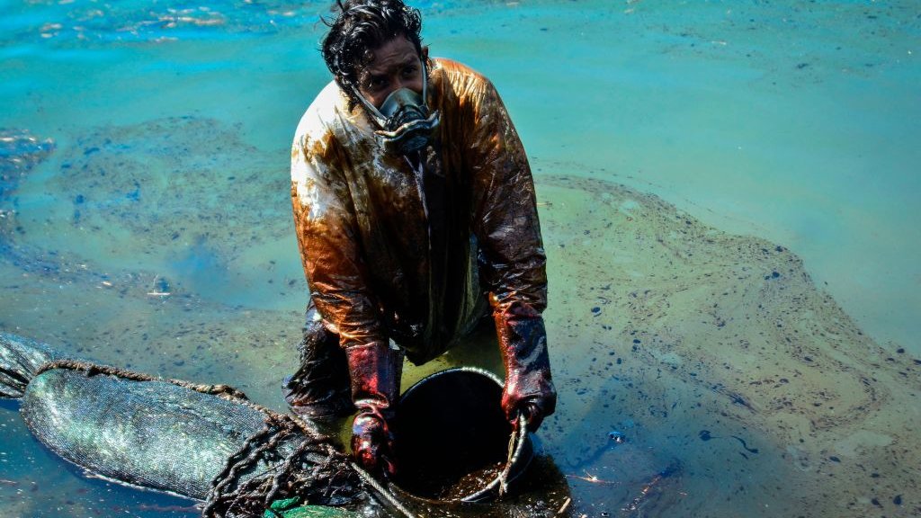 Мужчина убирает нефтяное пятно с пляжа