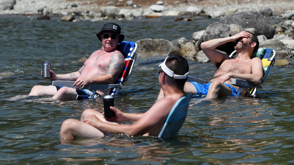 Beachgoers sit in the water at Alouette Lake to cool off during the scorching weather of a heatwave in Maple Ridge, British Columbia