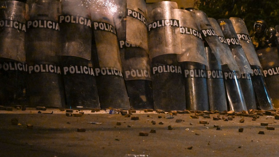 Policías protegidos por sus escudos, junto a adoquines lanzados por los manifestantes.