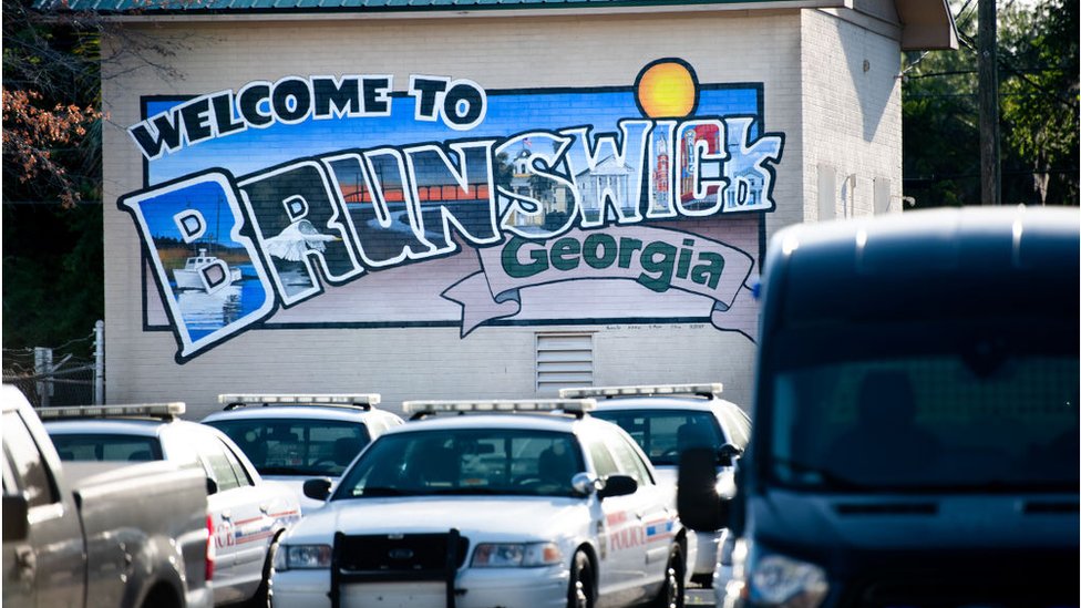 Фреска с надписью "Добро пожаловать в Брансуик, Джорджия" с полицейскими машинами впереди