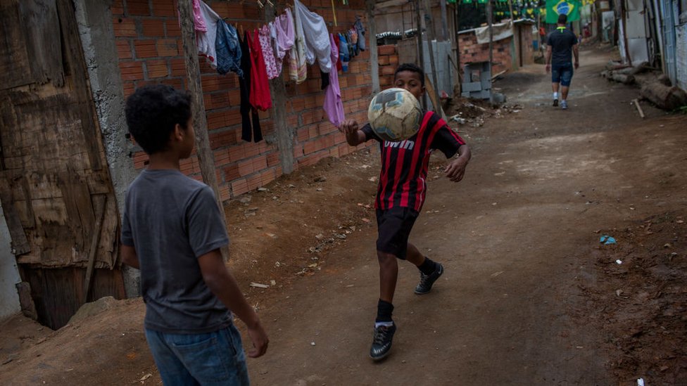 Niños jugando con una pelota de fútbol en una favela.