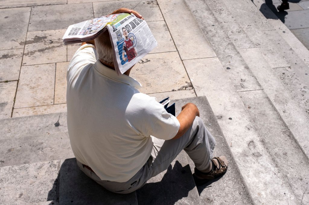 Man in a public square in London using a newspaper to shield himself from the harsh sun - 23 June 2023.