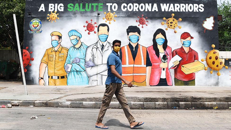 A man wearing a facemask walks past a Covid-19 mural in New Delhi , India - 31 May 2020