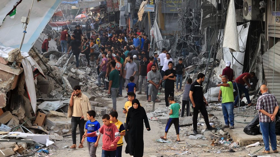 Palestinians walk amid the rubble of destroyed and damaged building in the heavily bombarded city centre of Khan Yunis 紀錄加薩in the southern Gaza Strip following overnight Israeli shelling, on 10 October 2023