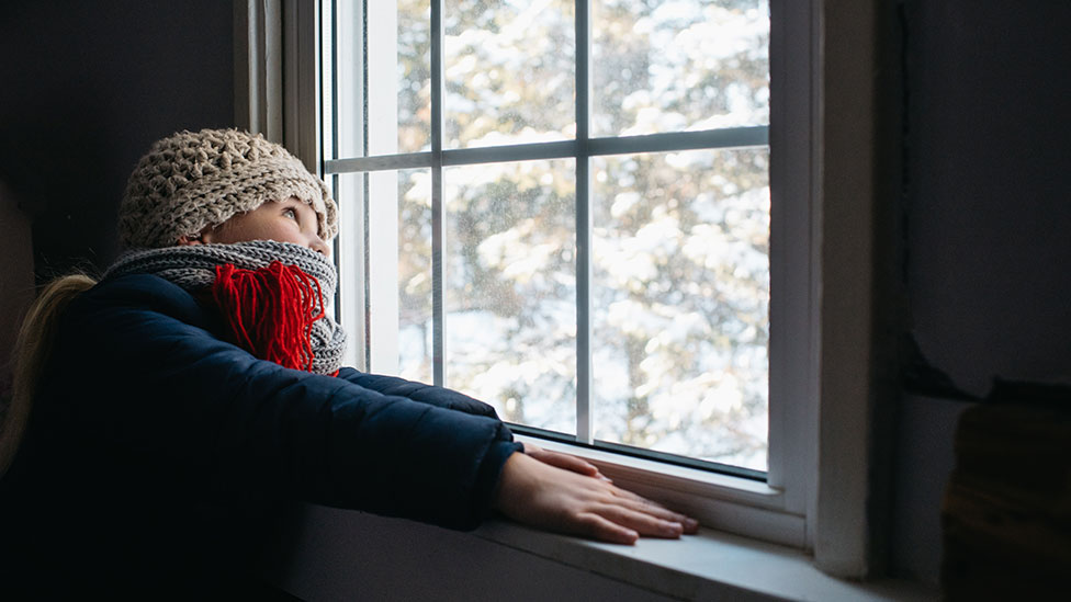 Girl looks out of window on cold day