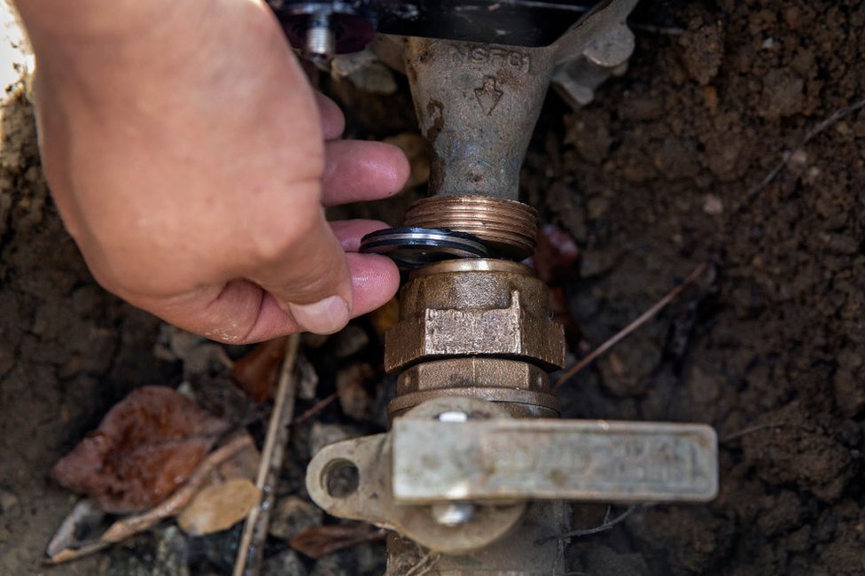Fernando González, del Distrito Municipal de Agua Las Vírgenes, instala un limitador de flujo en la toma de agua frente a una casa de Calabasas, California, el 2 de junio de 2022.