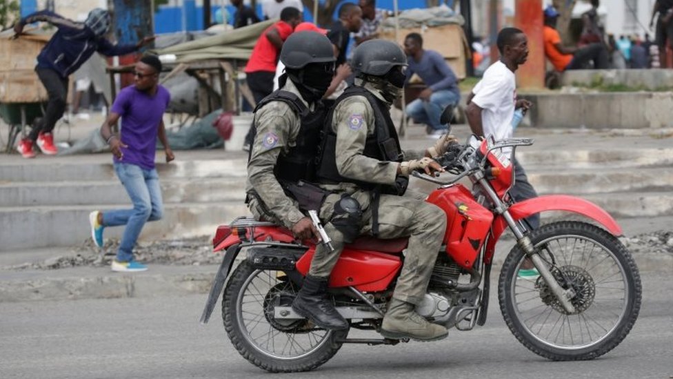 Protesters and masked men in Haitian National Police uniforms run away during a shooting in Champ de Mars, Port-au-Prince, Haiti February 23, 2020.