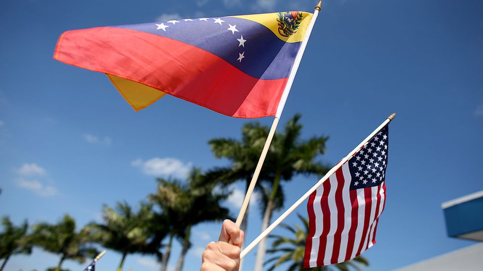 Una persona sostiene dos banderas, de Estados Unidos y Venezuela.