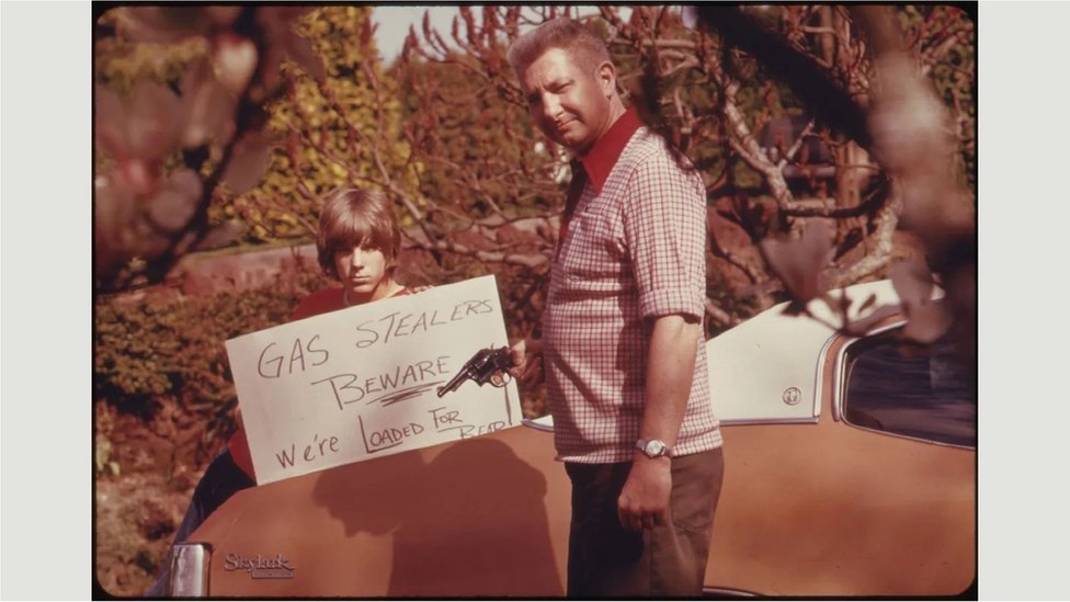 Pria memegang pistol dan tanda menentang pencurian bahan bakar