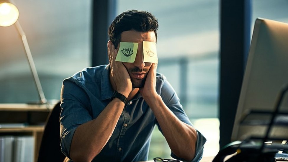 Quién sabe, tu próxima gran idea puede ocurrir cuando parezca que el mundo se detiene frente a tu computador. Un hombre sentado frente a la computadora, el rostro entre las manos, y dos post its en los ojos con dibujos de... ojos
