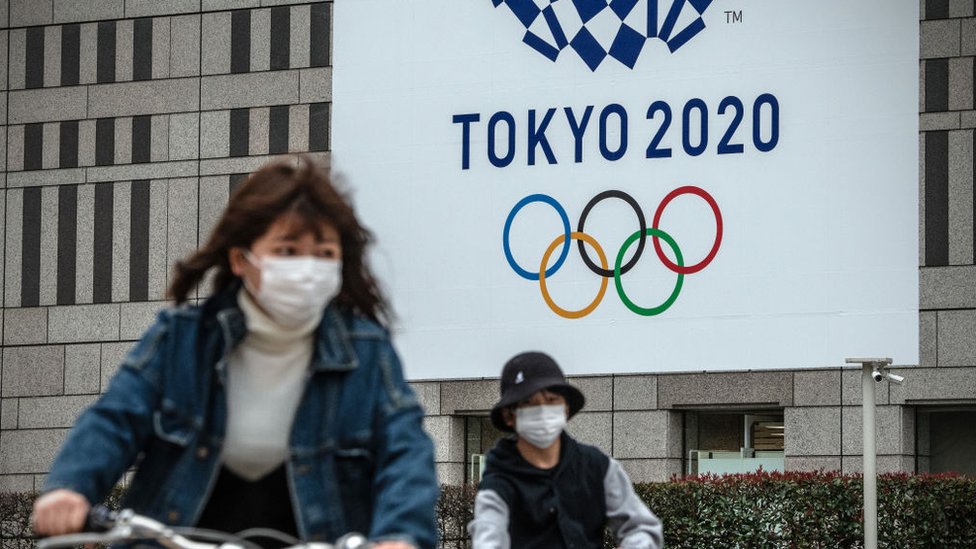 Japonesas en bicicleta pasan frente a la bandera olímpica en Tokio