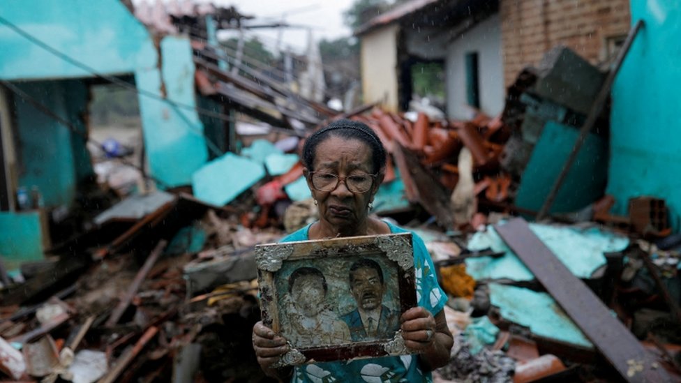 Imagen de una mujer frente a una residencia destruida