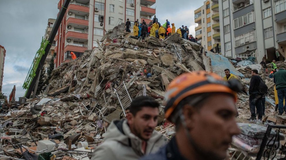 Un grupo de personas busca víctimas y sobrevivientes sobre los escombros de un edificio en la ciuad de Adana derrumbado por el terremoto