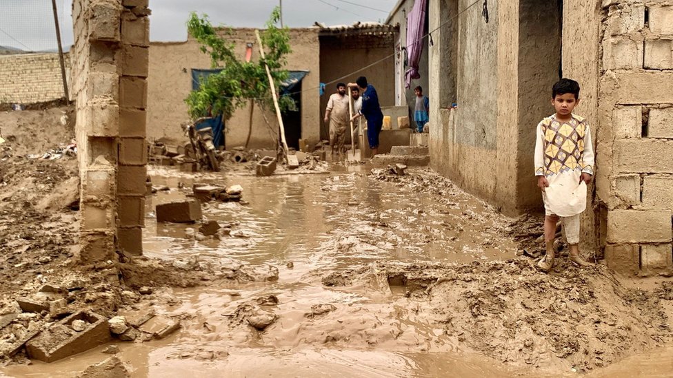 A boy looks on as people remove mud from the courtyard of their homes after floods in Maymana, Afghanistan, 19 May, 2024