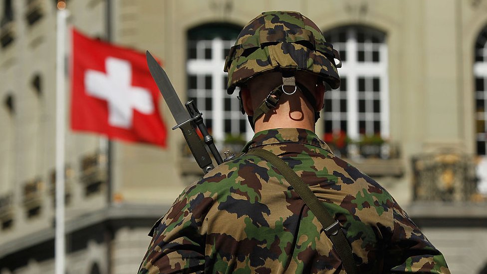 A Swiss soldier stands in front of a Swiss flag
