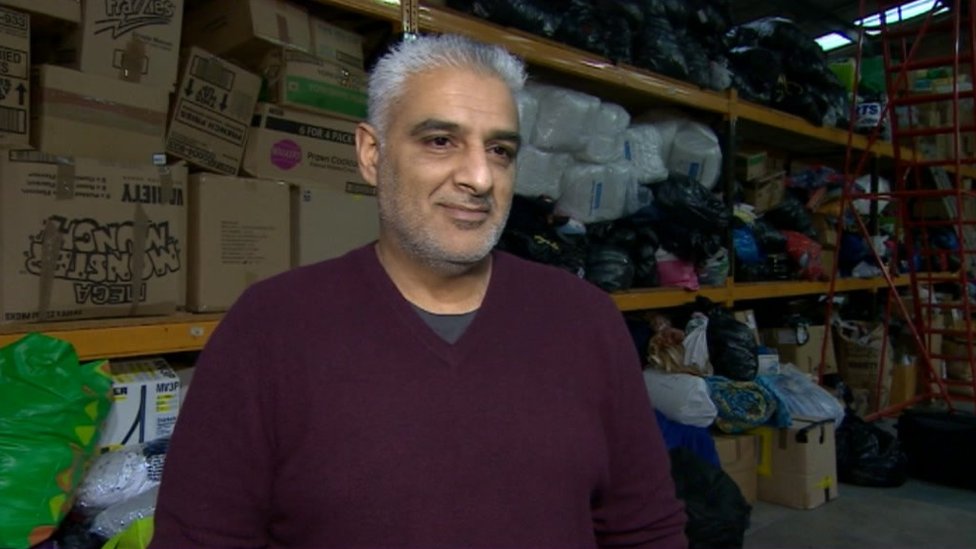 Tariq Jahan in front of piles of clothing and bedding donated by the public for migrants and refugees arriving in Greece