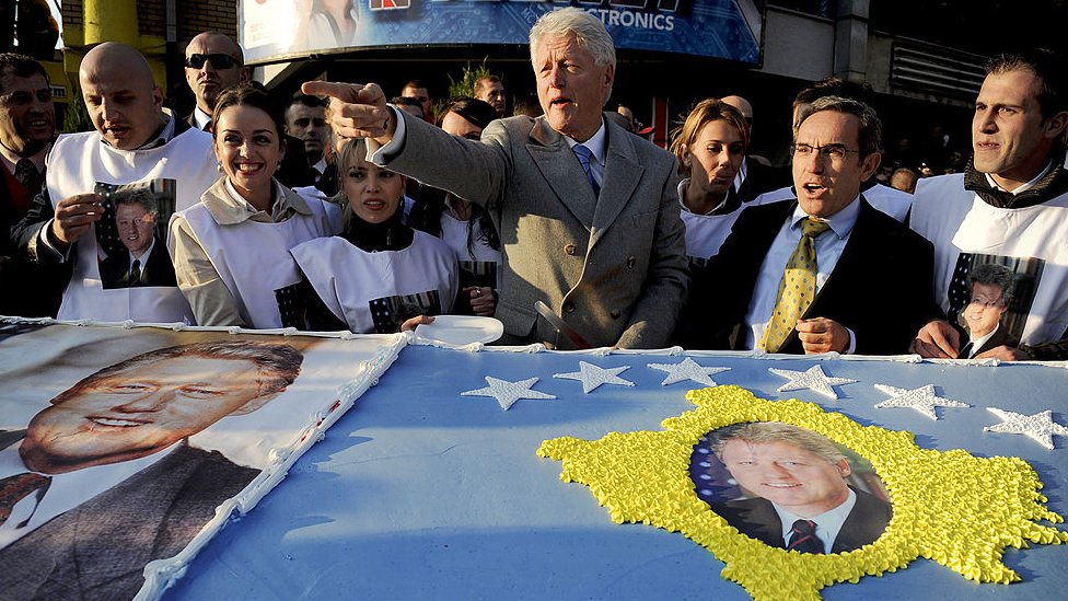 Бывший президент США Билл Клинтон приветствует косовских албанцев, стоя перед гигантским тортом, приготовленным для него во время его визита в Приштину 1 ноября 2009 г.