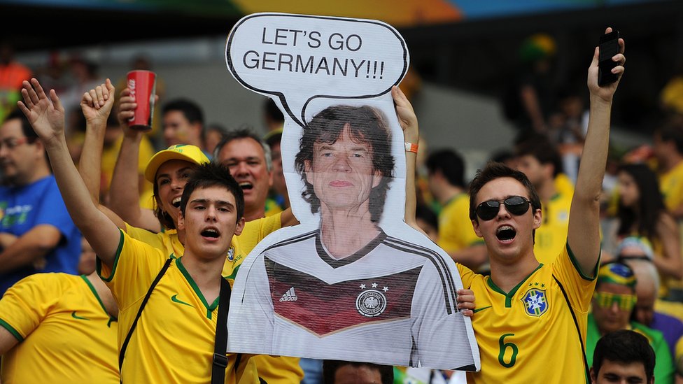 Hinchas de Brasil con una pancarta de Mick Jagger con la camiseta del equipo de Alemania.