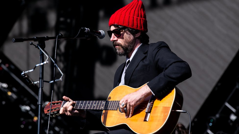 Графф Рис на сцене в красной шляпе и костюме играет на гитаре
