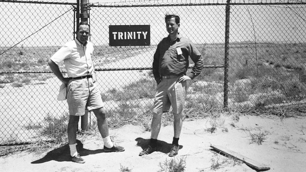 Dos hombres junto a un cartel de Trinity