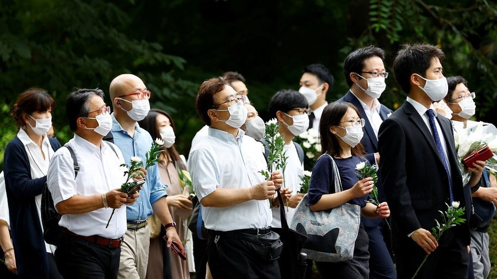 Warga memegang bunga sebagai tanda berduka di pemakaman Perdana Menteri Shinzo Abe di Kuil Zojoji, Tokyo, Jepang pada 12 Juli 2022.