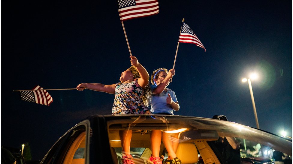 Children wave flags at a drive in social distance rally in Delaware