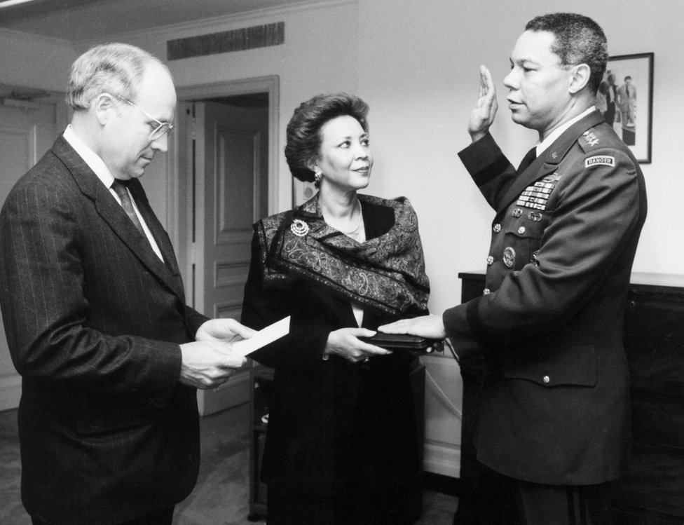 وزير الدفاع ديك تشيني (إلى اليسار) يعقد مراسم اليمين الدستورية للجنرال كولن باول كرئيس لهيئة الأركان المشتركة في عام 1989. زوجة الجنرال باول، ألما، تحمل الكتاب المقدس.
