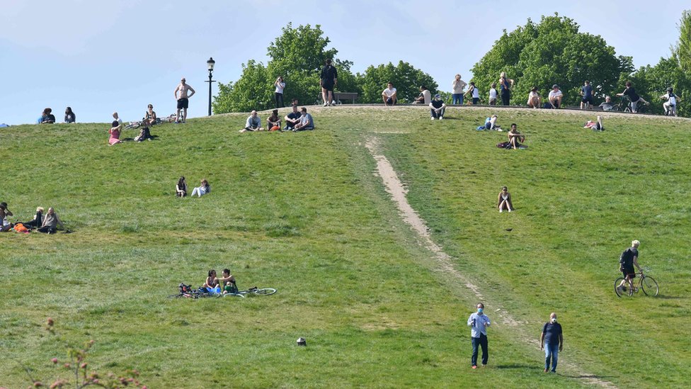 Люди озабочены тем, чтобы расслабиться на солнышке на Примроуз-Хилл в Лондоне 7 мая 2020 года, поскольку жизнь в Великобритании продолжается в условиях национальной изоляции, чтобы замедлить распространение нового коронавируса.