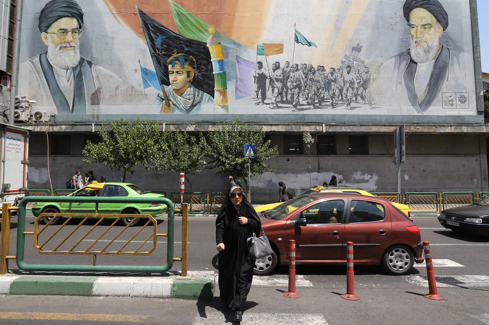 Иранская женщина проходит мимо фрески в Тегеране с изображением аятоллы Али Хаменеи (слева) и великого аятоллы Рухоллы Хомейни (справа) (25 июня 2019 г.)