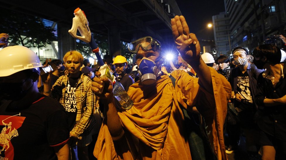 A monk wearing a gas masks flashes the three singer salute walk among pro-democracy protesters