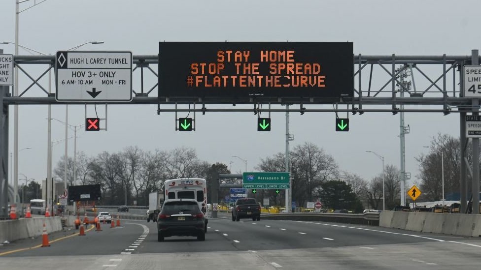 Автомобили проезжают под электронной вывеской, предупреждающей водителей о коронавирусе COVID-19, на шоссе возле моста Верразано 30 марта 2020 года в Нью-Йорке.