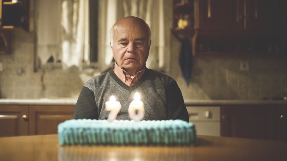Hombre mayor contemplando una tarta de cumpleaños con dos velas que ponen 70