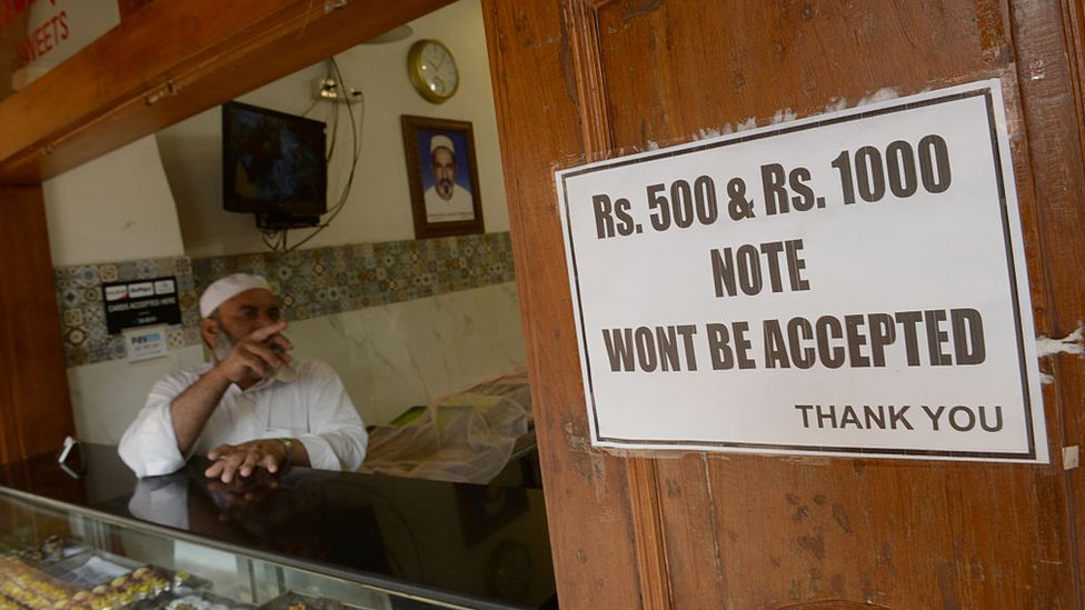Владелец магазина в Мумбаи показывает уведомление о непринятии старых банкнот по 500 и 1000 рупий