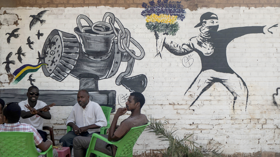 أناس يحتسون الشاي بالقرب من جدارية تحاكي أسلوب بانكسي، رسام الغرافيتي البريطاني.