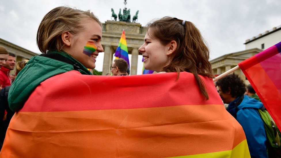 Две женщины, закутанные в радужный флаг на митинге в Германии