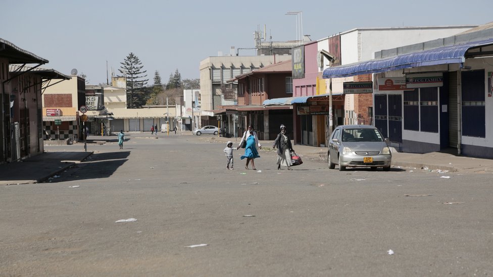 Женщины и ребенок гуляют по безлюдной улице и закрытым магазинам за день до антиправительственных протестов в центральном деловом районе Хараре, Зимбабве, 30 июля 2020 года.