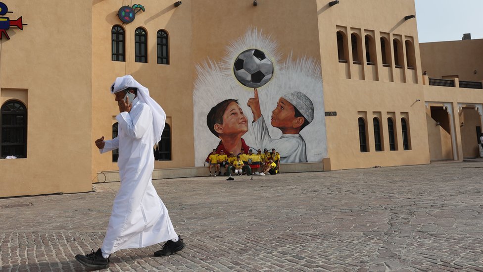 Hinchas ecuatorianos frente a un edificio con una pintura de niños y una pelota.