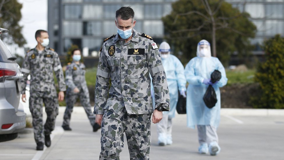Солдат в маске выходит из дома престарелых с другими медицинскими работниками
