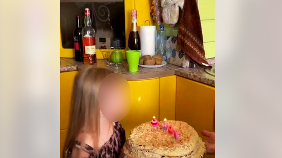 Uma menina (com o rosto borrado) apaga as velas de um bolo de aniversário na cozinha amarela