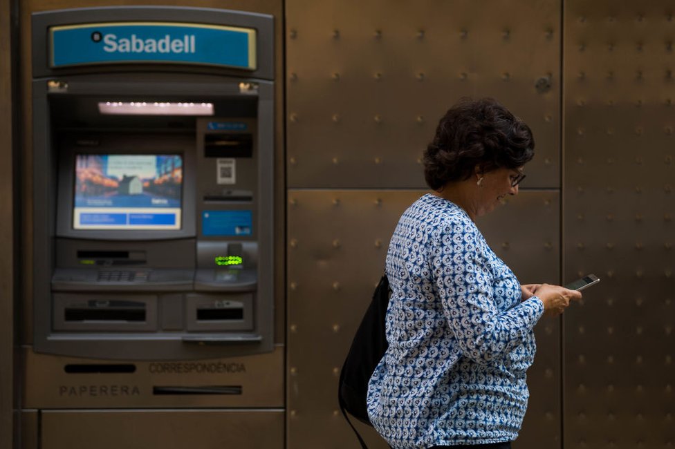 El Banco Sabadell anunció que se trasladará de Cataluña para preservar los intereses de sus clientes. Mujer frente a un cajero del Banco Sabadell en Barcelona.
