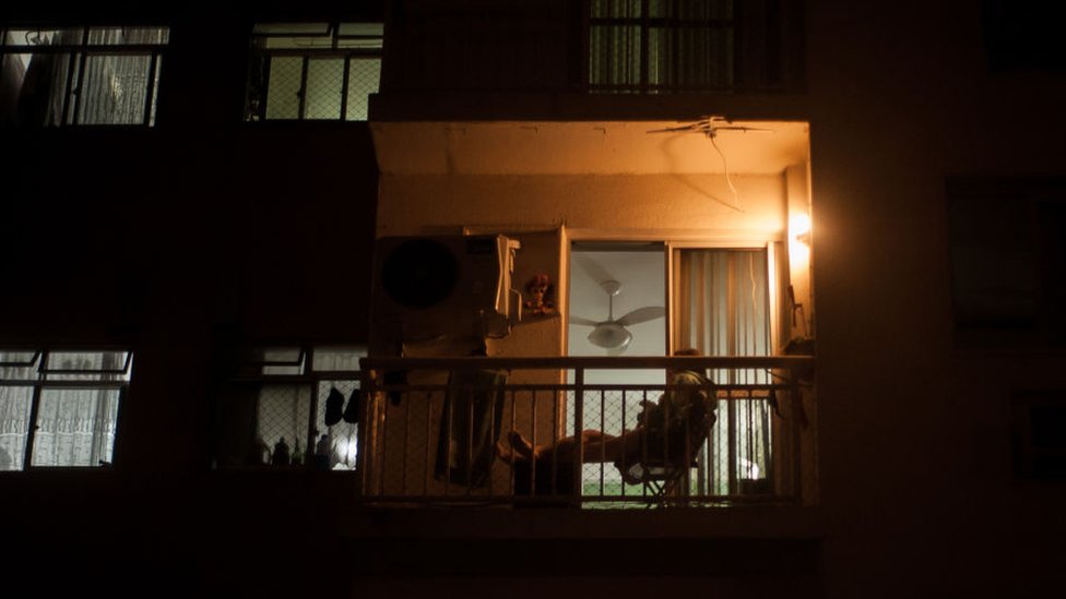 Contorno de pessoa em varanda de apartamento à noite